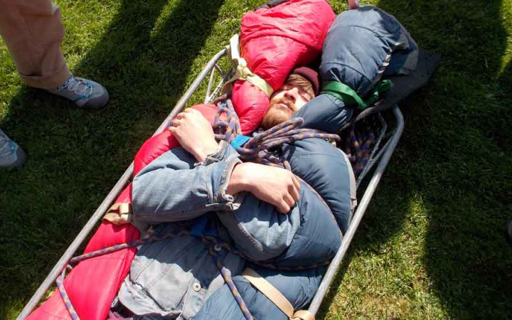 a person lies in a stretcher during a wilderness first aid training